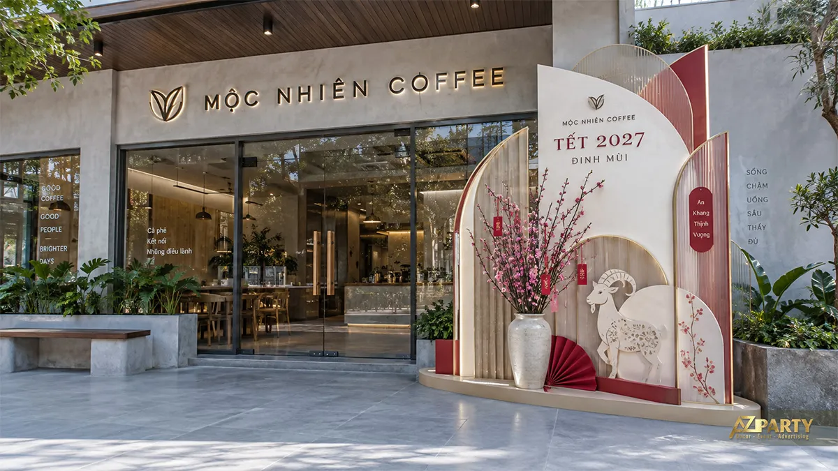Backdrop Tết trước quán cà phê với các lớp vòm kem đỏ, linh vật dê và bình hoa đào