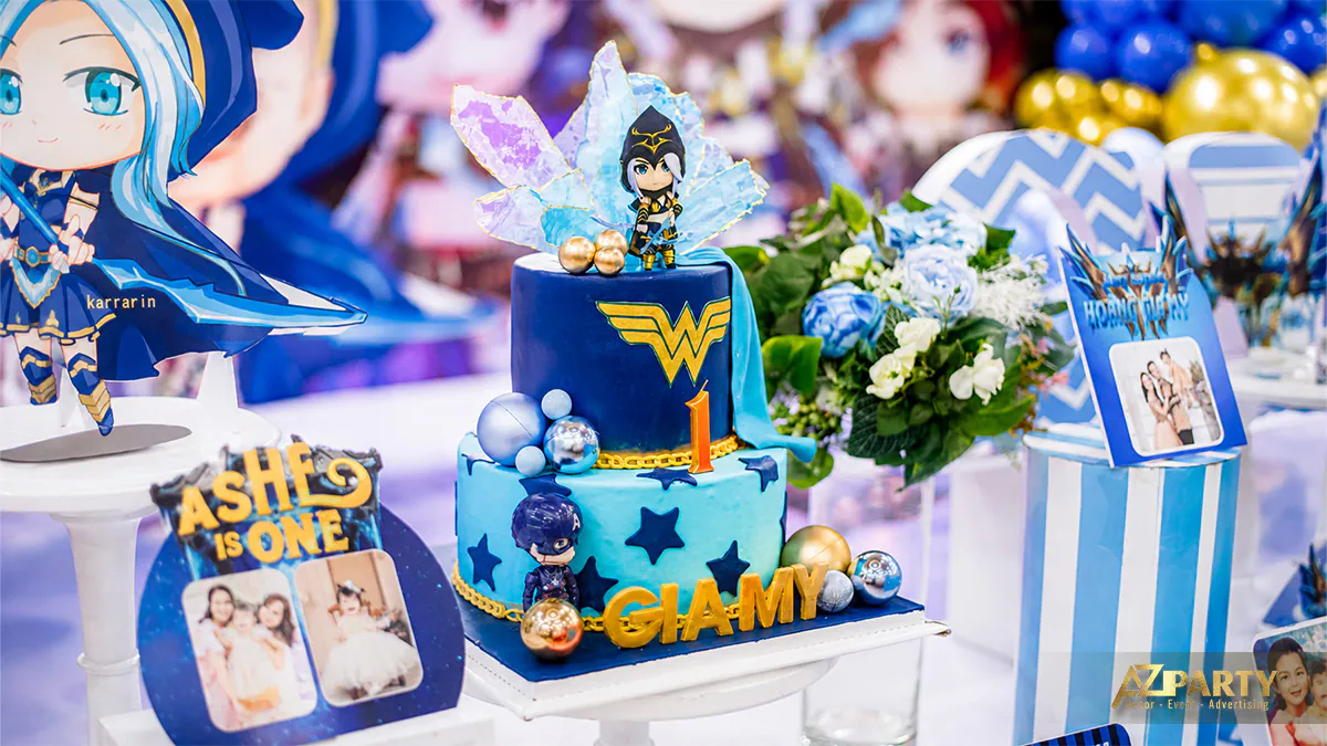 Bánh kem sinh nhật 2 tầng màu xanh dương chủ đề siêu anh hùng và game Liên Quân với tên bé 'Gia My' nổi bật, phía trên là mô hình mini Tel'Annas.