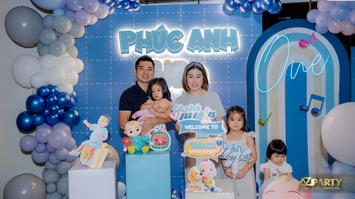 Khách mời chụp ảnh lưu niệm cùng gia đình trước phông nền sự kiện màu xanh bắt mắt