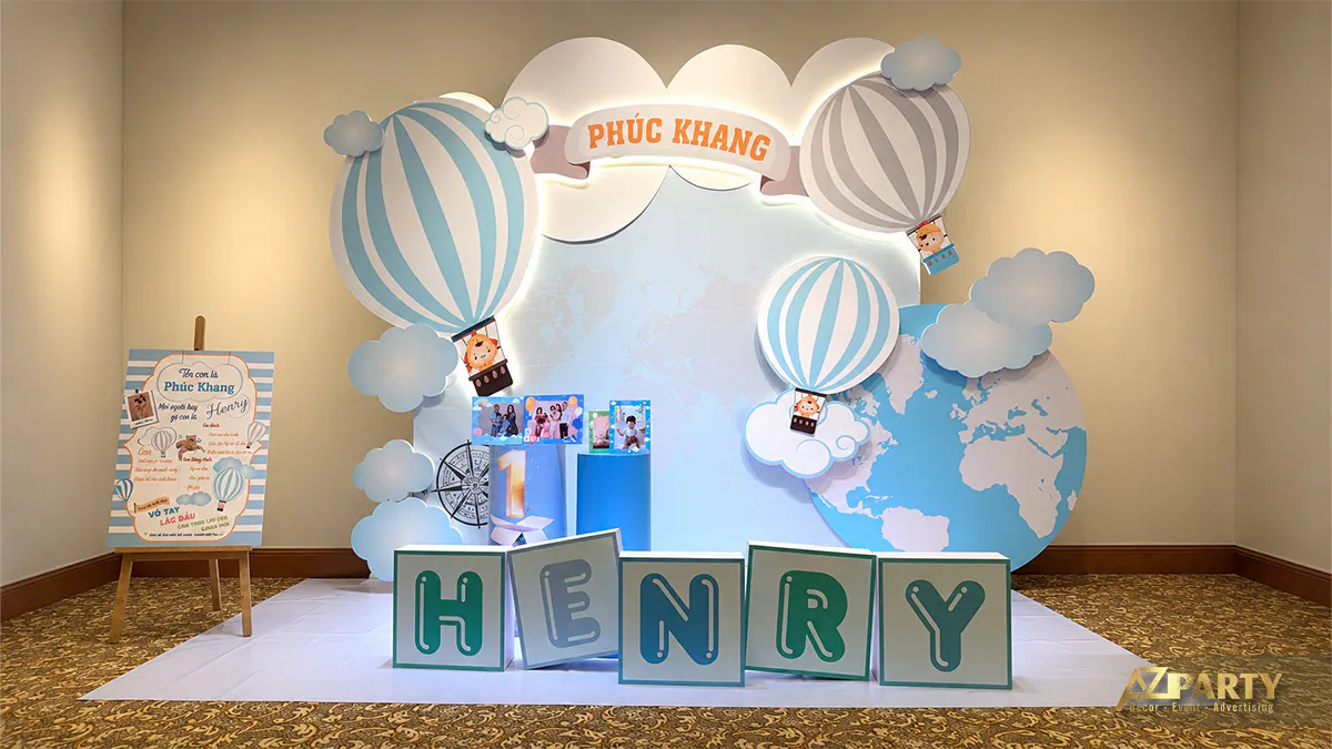 Không gian photobooth thôi nôi bé Phúc Khang nổi bật với mô hình chữ HENRY 3D màu xanh ngộ nghĩnh đặt trên thảm trắng