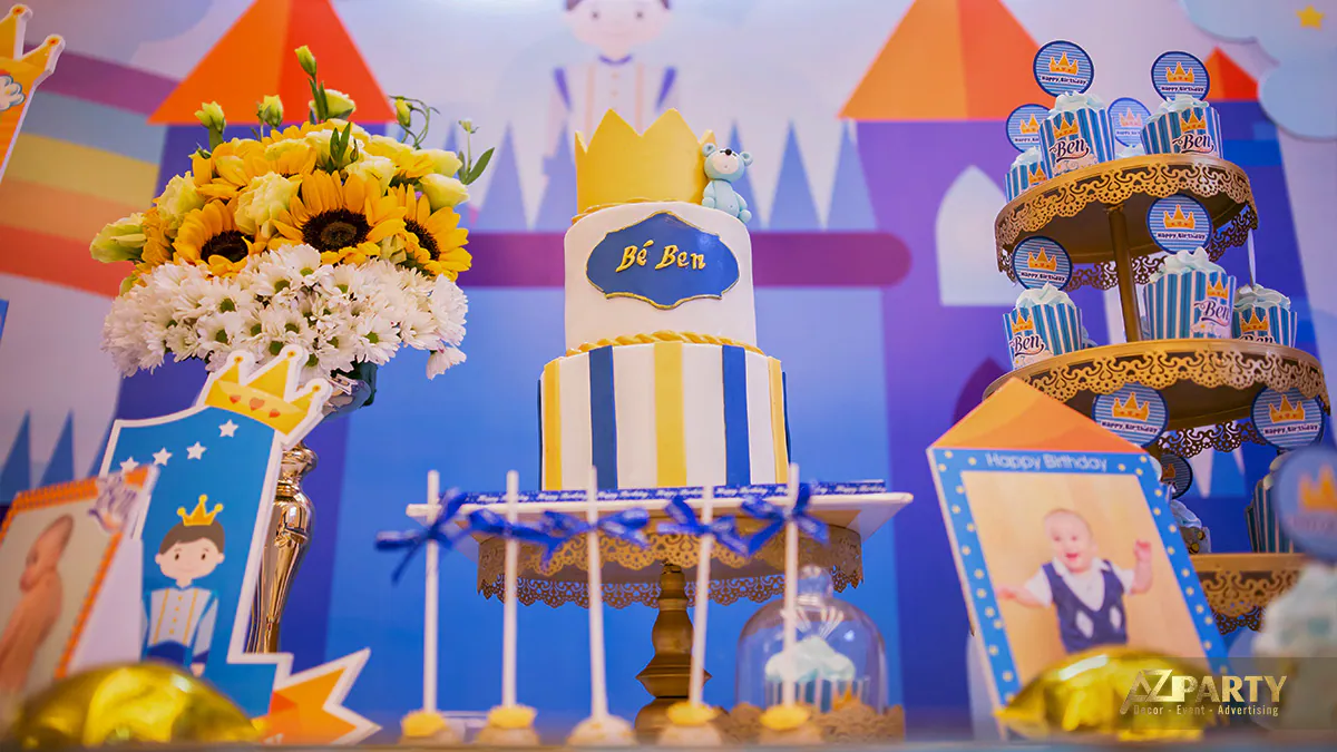 Bánh kem hai tầng độc đáo vẽ tên Bé Ben với vương miện vàng cùng tháp bánh cupcake xinh xắn tại tiệc thôi nôi