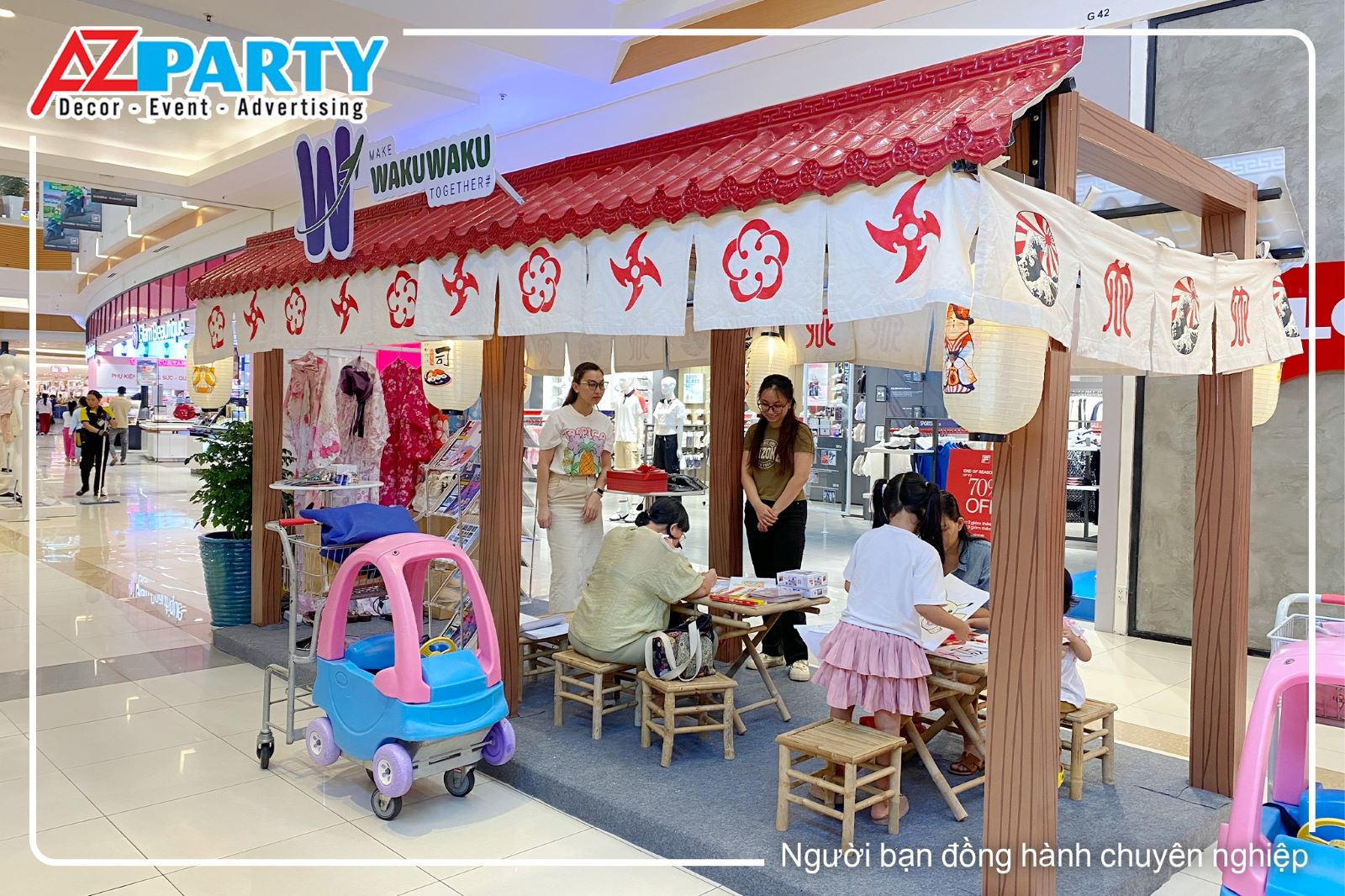 Góc chụp bên hông của booth có logo trên mái và rèm hình hoa đào, phi tiêu