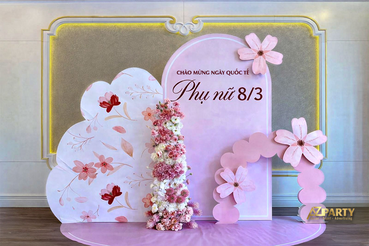 Mẫu backdrop trang trí 8/3 xinh với tone hồng pastel chủ đạo, thiết kế vòm mềm mại kết hợp mảng hoa in nghệ thuật và cụm hoa lụa 3D nổi bật ở trung tâm.