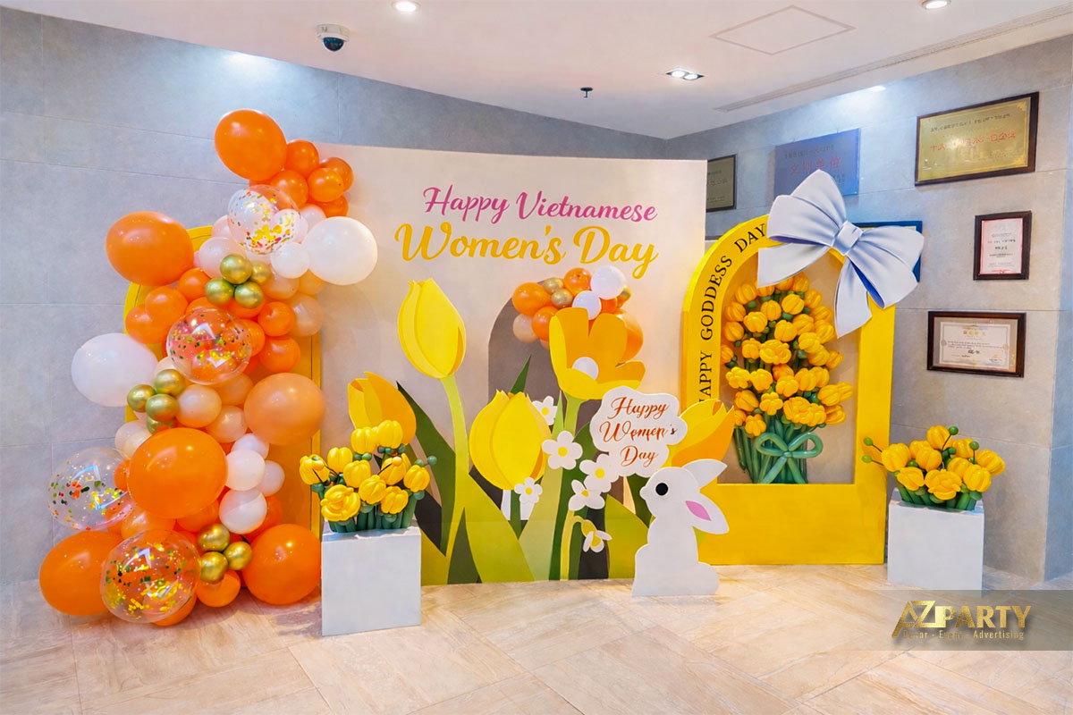 Backdrop trang trí 8/3 tông vàng cam rực rỡ với bóng bay nghệ thuật, hoa tulip, khung vòm lớn và chữ “Happy Vietnamese Women’s Day”