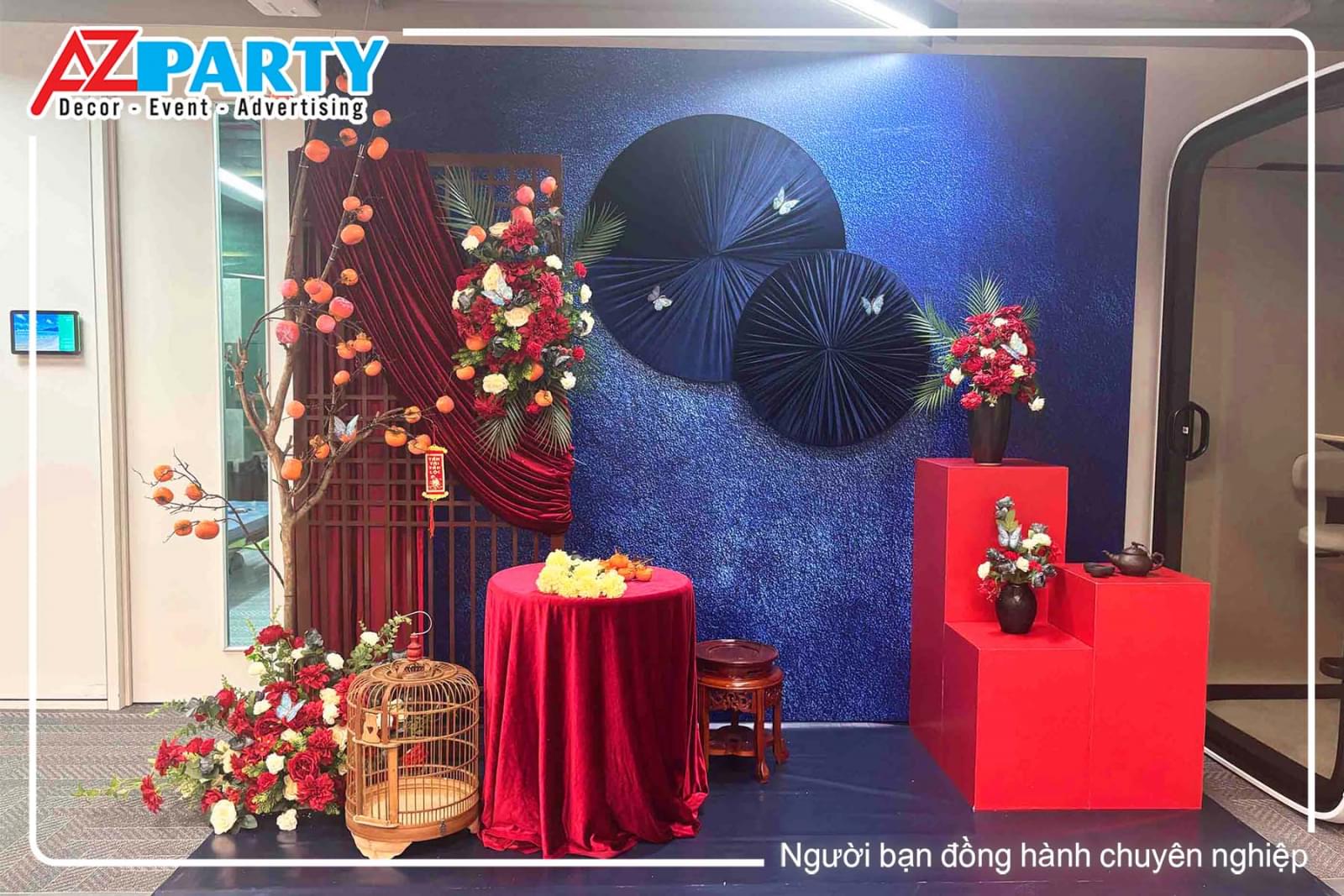 Tiểu cảnh tết thanh lịch Á Đông với phông nền xanh dương sang trọng, vải nhung đỏ, cành hồng kết hợp hoa xuân, quạt trang trí, bàn trưng bày và bục decor tinh tế.
