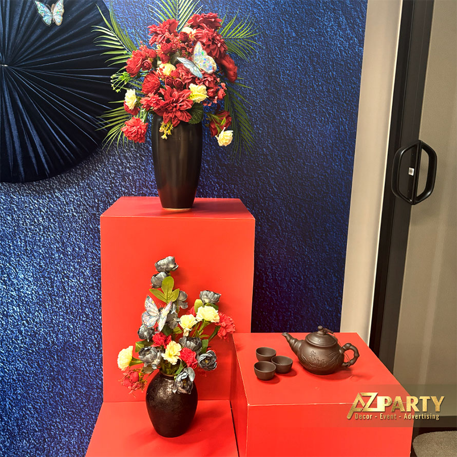 Chi tiết tiểu cảnh Tết với khối trưng bày màu đỏ, bình hoa Tết phối đỏ, vàng và bình gốm đen và bộ ấm trà