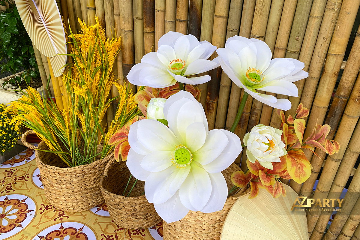 Giỏ mây đựng lúa vàng và hoa sen trắng trang trí Tết đặt trước nền tre trúc, kết hợp quạt lá và họa tiết gạch bông truyền thống.