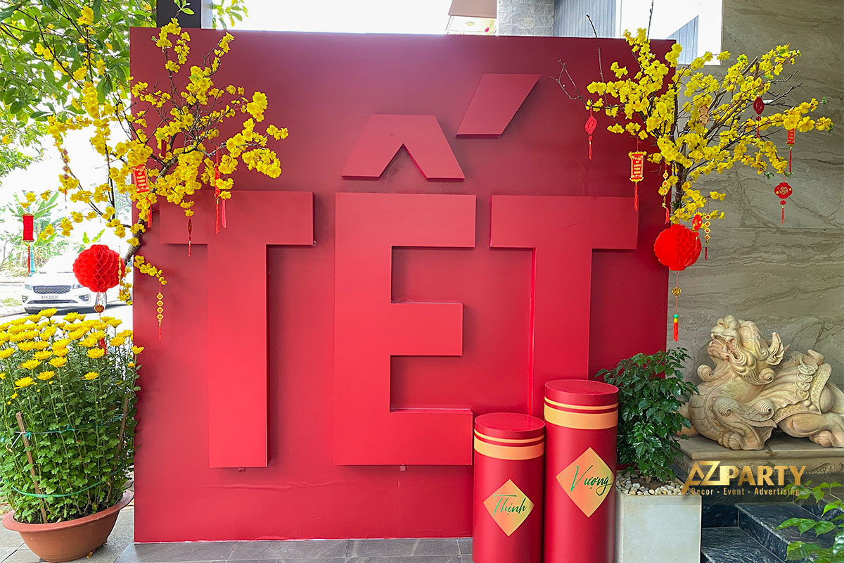 Tiểu cản Tết màu đỏ nổi bật với chữ “TẾT” 3D, trang trí cành mai vàng, đèn lồng đỏ và trụ pháo đỏ trong không gian sảnh văn phòng.