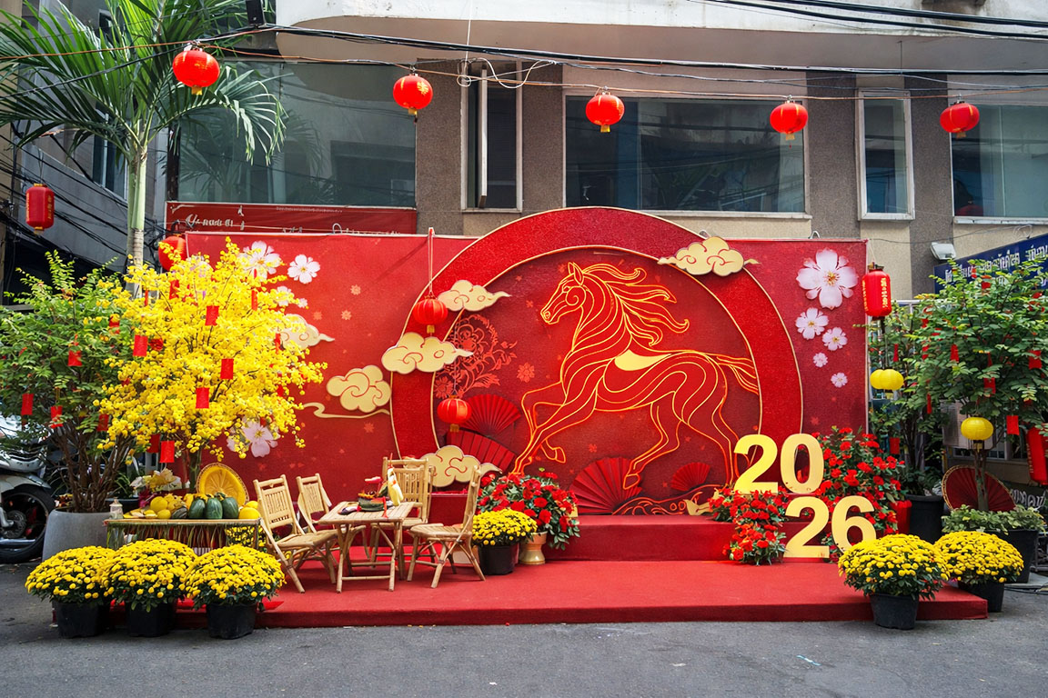 Tiểu cảnh trang trí Tết ngoài trời với phông đỏ chủ đề ngựa cách điệu, đèn lồng treo, hoa mai vàng, bàn ghế tre