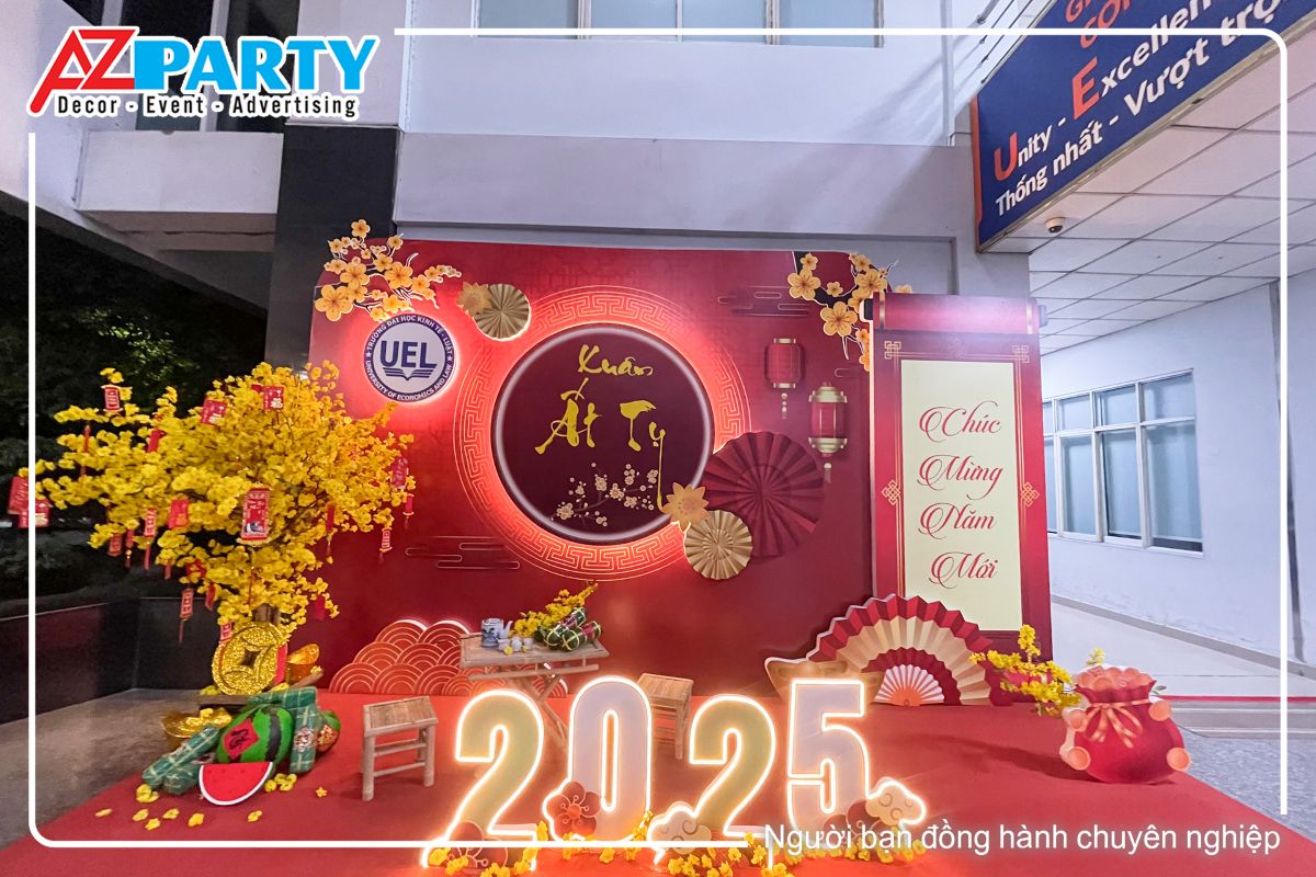 Tiểu cảnh tết tại trường dại học kinh tế luật, với tone màu đỏ. Nổi bật tại tiểu cảnh là cây mai vàng, bộ chữ 2025 với đèn neon vàng