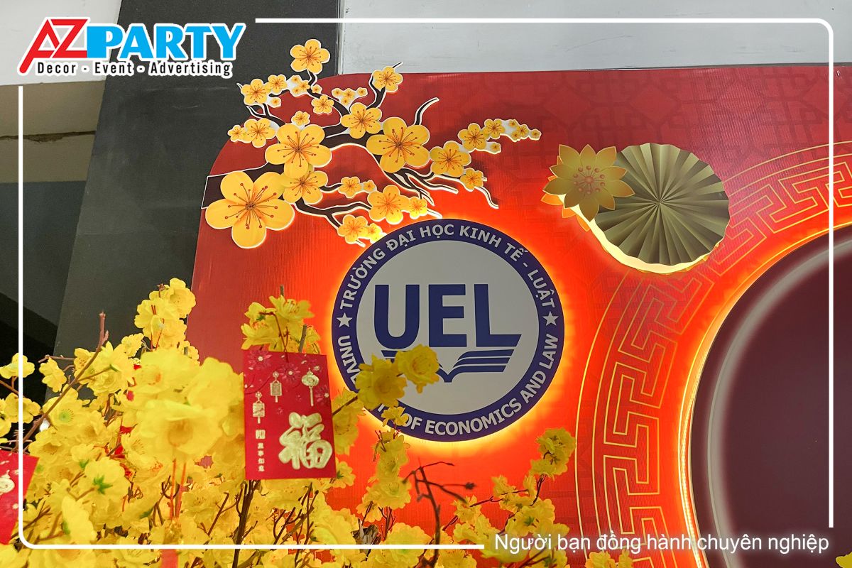 Logo thương hiệu trường đjai học kinh tết luật tại góc trái của backdrop, trên cùng là cành hoa mai vàng